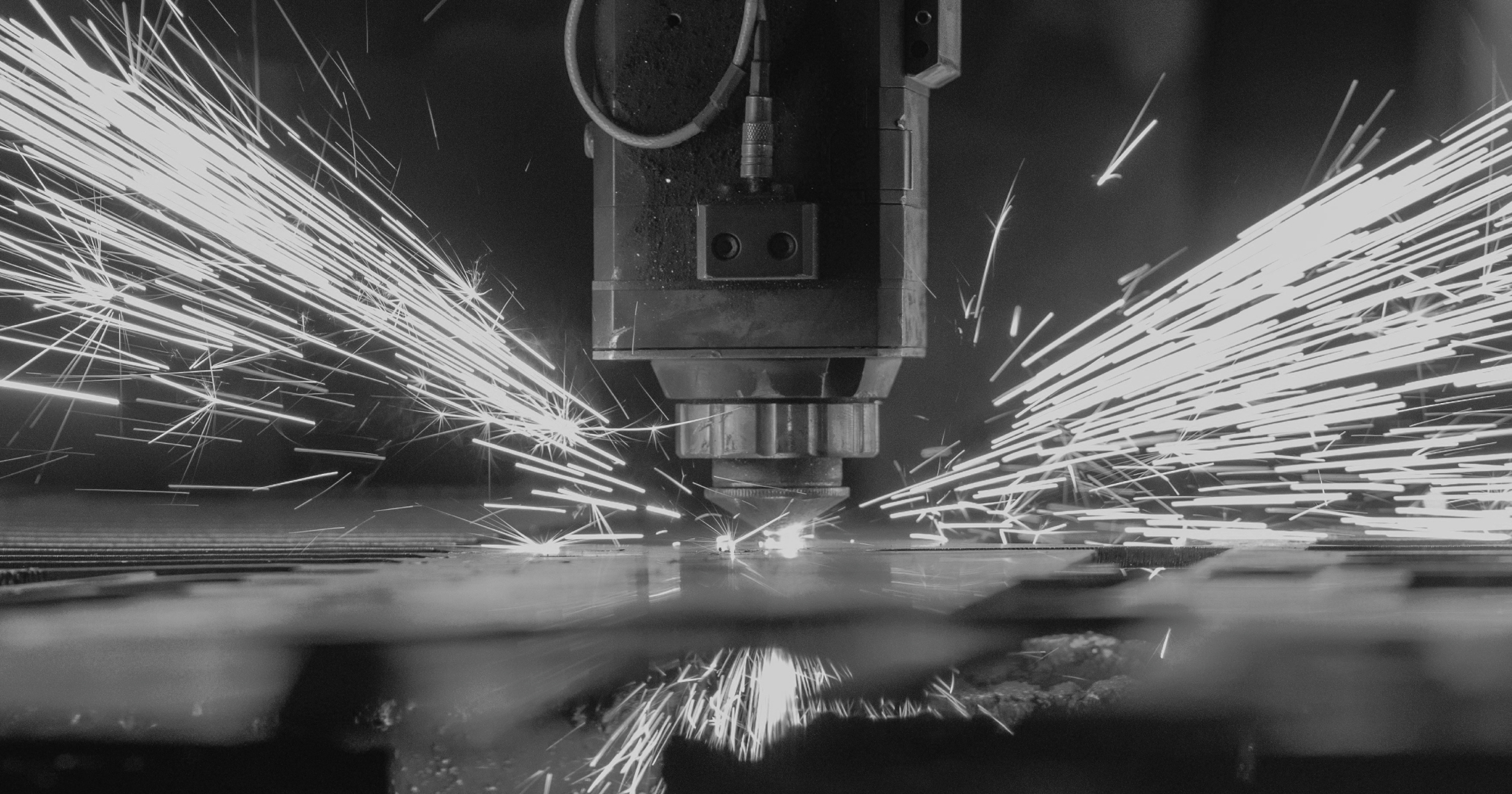 Black and white image showing a CNC machine live-milling a workpiece. Sparks are flying out of the workpiece as the milling cutter works through the material.