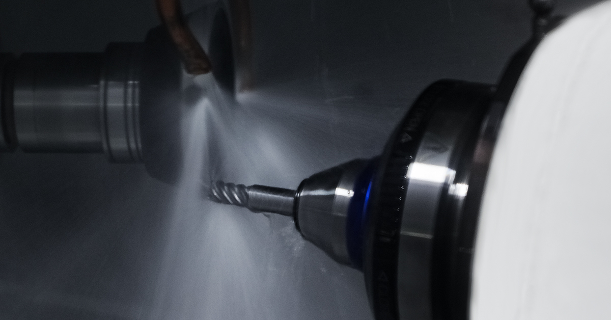 Coolant flooding the cutting edge of a solid carbide end mill during a regrind pass on a 5-axis tool grinder.