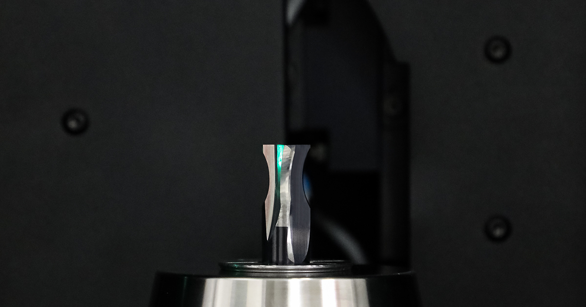 A solid carbide end mill mounted on optical measuring equipment, captured mid-scan as the ground edges are checked.